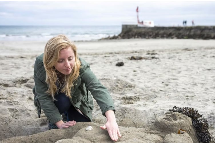An art student making a sand sculpture on the beach at East Looe with the Banjo Pier in the background.