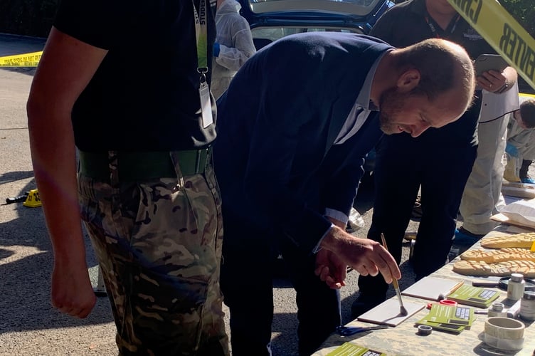 The Prince dusting a fingerprint at the forensic crime scene set up by the Maps students studying military services at Duchy. (Picture: Sarah Martin)