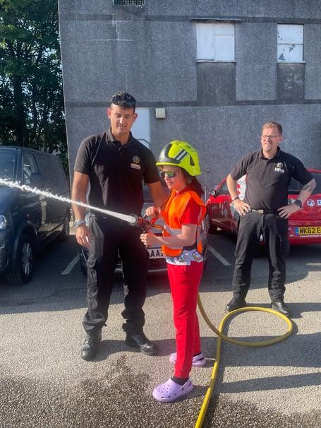These young member of the 1st Liskeard Rainbows tries her hand at working the hose with Liskeard Community firefighters