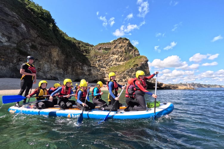 Children taking to the sea on a large stand up paddleboard during a summer camp at Porthpean in Cornwall.