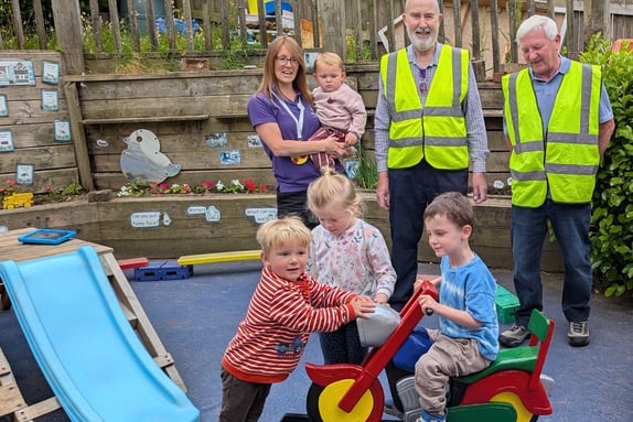 Looe Shedders Chairman Chris Roy and Assets Manager Bob Baber present the restored rocking motorbike to children at Barbican Preschool.