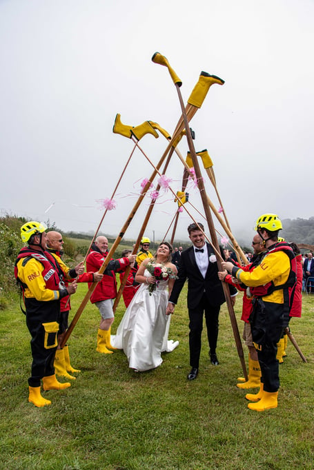 Amber and Alex Richardson walking through Looe RNLI’s yellow welly guard of honour after their marriage.